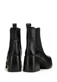 Botas de tobillo de cuero negro con un acabado texturizado, paneles laterales elásticos y un tacón negro grueso y estratificado. Cuenta con tiradores para facilitar su colocación.
