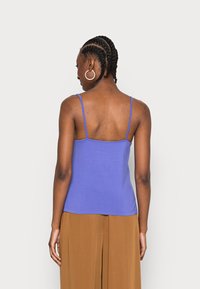 Top de tanque sem mangas roxo, com alças finas, design justo, textura suave e costas em formato de scoop, combinado com calças largas bege.