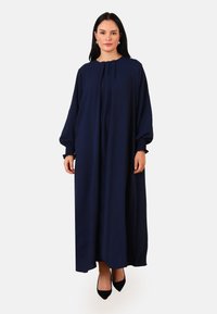 Robe maxi bleu marine à manches longues, décolleté plissé et poignets froncés. Fabriquée en tissu léger ; texture douce, design simple.