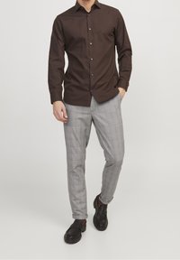 Mörkbrun långärmad skjorta med knappar, kombinerad med grå rutiga byxor och svarta loafers. Skjortan har en krage och knappar, medan byxorna har en slim fit.