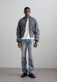 Hallhalli hall jacket ribade jaotustega, valge T-särk, heledad sinised kitsad teksapüksid tekstuursete aktsentidega ja mustad jalanõud. Lihtne ja modernne disain.
