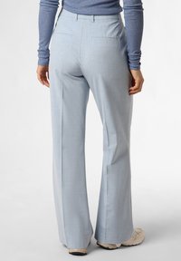 Pantalones de pierna ancha en azul claro con un acabado texturizado, que cuentan con bolsillos en la parte posterior y una cinturilla entallada. Combinados con zapatillas beige.