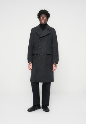 Abrigo de doble botonadura en gris oscuro, mezcla de lana, con amplios cuellos con muesca, dos bolsillos delanteros, cierres de botón, combinado con pantalones y zapatos negros.
