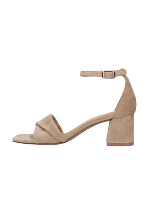 Beige suède hakken sandaal met een open neus en een kruislings ontwerp. Bevat een verstelbare enkelband en een chunky hak.