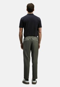 Marineblauw poloshirt met korte mouwen, gecombineerd met olijfgroene broek met een koord in de taille en twee achterzakken. Sneakers met witte en zwarte accenten.