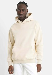 Sudadera beige de tejido suave, con un bolsillo frontal, capucha con cordones y un discreto logo bordado. Ajuste casual y relajado con puños acanalados.