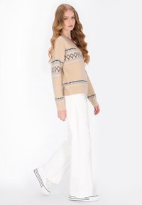 Beżowy sweter w geometryczne wzory w granatowym i jasnoniebieskim kolorze. Połączony z białymi szerokimi spodniami i sneakersami w czarne paski.