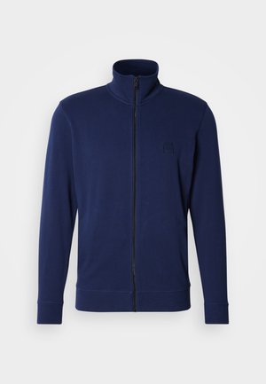 Tamsiai mėlynas džemperis su užtrauktuku, aukštu apykakliu, ilgomis rankovėmis, raštuotais rankogaliais ir mažu įspaustu logotipu kairiajame krūtinės plote, pagamintas iš lygios medžiagos.