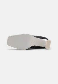 Zapato negro con parte superior de cuero suave, suela de goma blanca y tacón texturizado. La suela es plana y ligeramente contorneada para mayor comodidad.