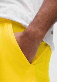 Klart gula sportshorts gjorda av mjukt tyg, med en sidofick. Bärs med en texturerad vit skjorta, vilket visar en avslappnad stil.