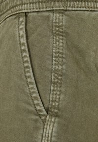 Tissu en mélange de coton vert, présentant une texture à côtes verticales, avec des coutures détaillées et une poche latérale.