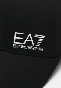 Texturált anyagból készült fekete sapka, amelyen a "EA7 EMPORIO ARMANI" feliratú fehér logó található. Egyszerű, strukturált dizájn, ívelt karimával.