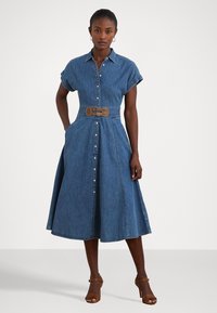 Denim skjortekjole med korte, oppbrettede ermer, knapplukking foran, belte i midjen med brun spenne, og flytende A-linjekjole.