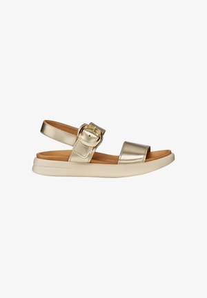 Gold metallic open-toe sandal with ankle strap, large round buckle, cushioned tan footbed, and thick white sole.