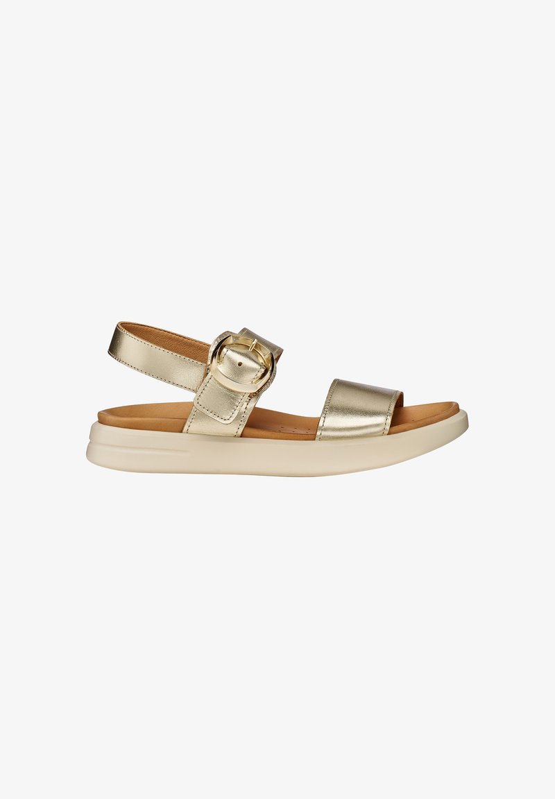 Gold metallic open-toe sandal with ankle strap, large round buckle, cushioned tan footbed, and thick white sole.