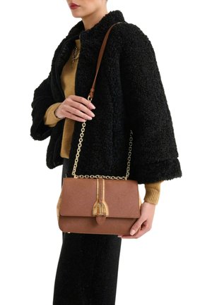 Borsa marrone con trama, dotata di una tracolla a catena dorata, con una chiusura distintiva e dettagli beige, tenuta da una persona con una giacca nera pelosa.