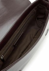 Interno della borsa in pelle marrone, con una texture liscia, tasca con zip e fodera in tessuto marrone. Design minimalista con cuciture robuste.