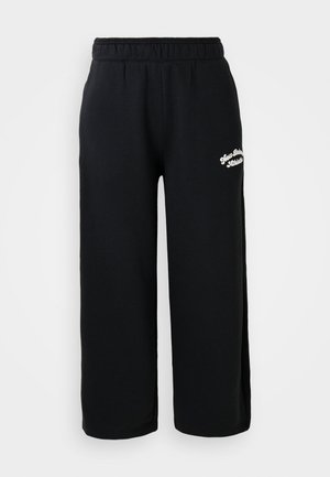 Pantalon de survêtement noir en coton doux, avec une taille élastique et une coupe cropped. Petit texte brodé blanc sur le côté.