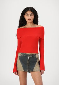 Top a coste rosso off-the-shoulder con maniche lunghe, abbinato a una gonna di jeans corta con zip anteriore e design a patchwork a contrasto.