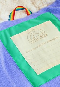 Paarse fleece jas met een groen label van stof waarop een regenboogontwerp en een lijst voor namen staan. Meerkleurig hangerlint bevestigd.