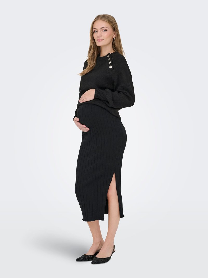 Nėščia moteris juodu megztiniu su sagomis ant peties ir juodu ribuotu sijonu su šoniniu skeltuku, stovinti ir laikanti savo pilvą.