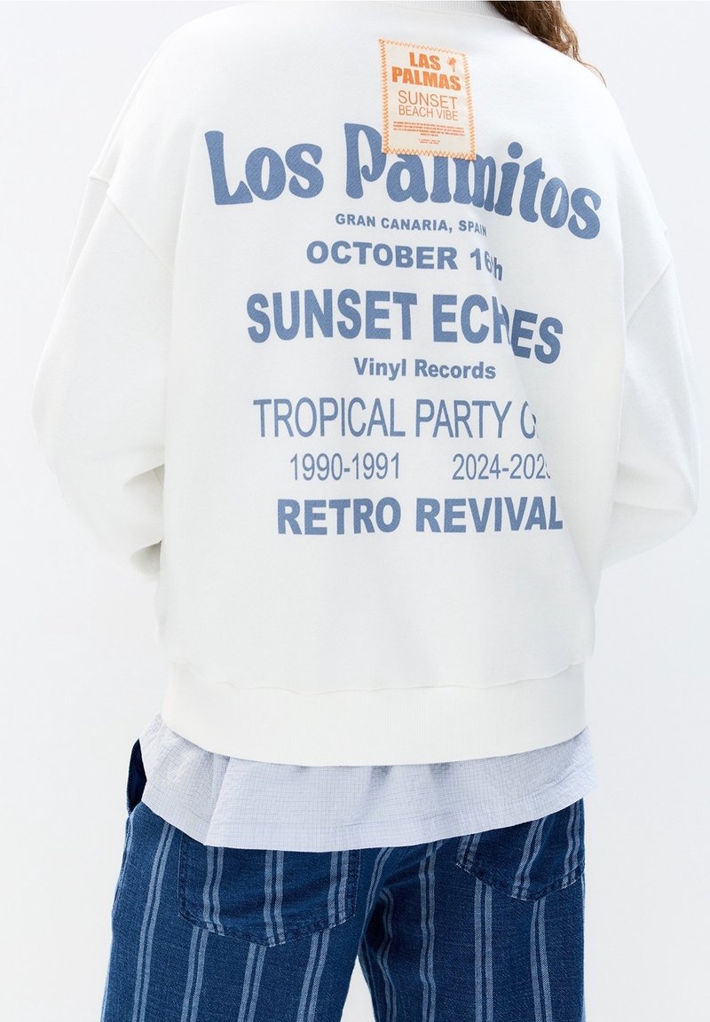 Sweat-shirt blanc avec texte bleu faisant la promotion de la fête tropicale "Los Palmitos Sunset Echoes" à Gran Canaria, le 16 octobre, sur le thème du revival rétro.