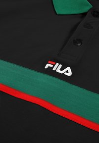Zwart poloshirt met een groene kraag, voorzien van een horizontale groene en rode streep en het geborduurde "FILA" logo in het wit. Geleefd textiel.