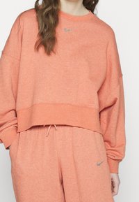 Coral sweatshirt with a cropped design, long sleeves, and a rounded neckline. Features a rhinestone-embellished logo on the chest.