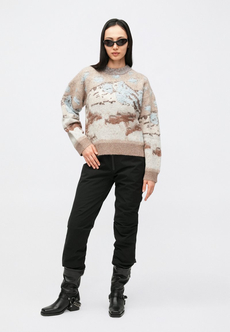 Maglione con motivo beige, blu e marrone, realizzato in tessuto morbido. Abbinato a pantaloni aderenti neri e stivali neri al ginocchio.