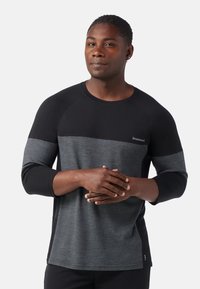 Langärmliges Shirt mit einem Farbblockdesign in Schwarz und Dunkelgrau, aus weichem Stoff gefertigt. Verfügt über Raglanärmel und ein Logo auf der Brust.