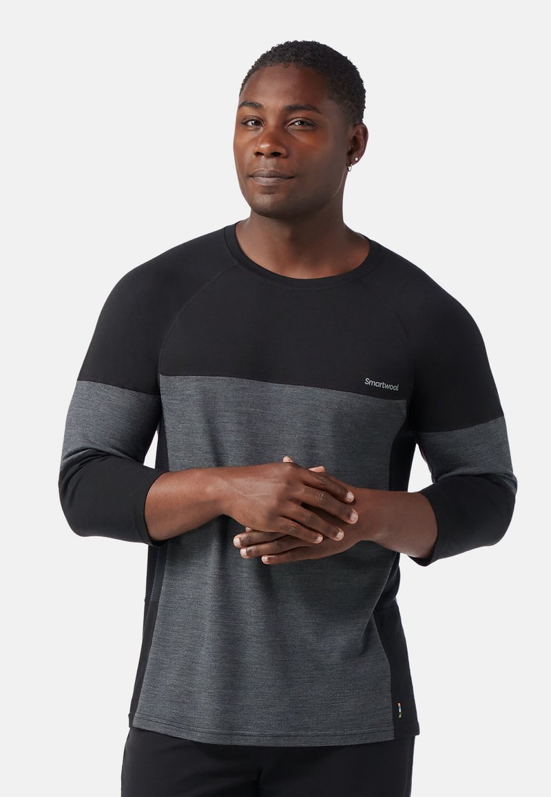 Langärmliges Shirt mit einem Farbblockdesign in Schwarz und Dunkelgrau, aus weichem Stoff gefertigt. Verfügt über Raglanärmel und ein Logo auf der Brust.