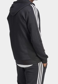 Felpa nera con design a tre strisce bianche sulle maniche, realizzata in tessuto morbido, con vestibilità comoda e tasca a marsupio.