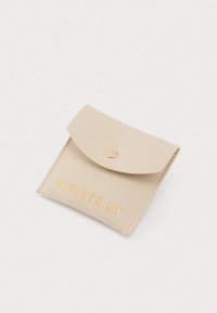 Beige ruskinds firkantet møntpung med fold-over klap og guld trykknap, prydet med "GINETTE NY" i guldbogstaver.