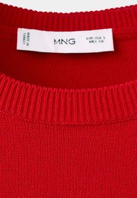 Col de pull en maille rouge avec une étiquette blanche indiquant la marque MNG, la taille EUR-USA S, MEX CH, et le texte Fabriqué en Turquie.