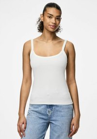 Top de tirantes blanco acanalado con tirantes anchos y escote cuadrado; combinado con jeans de mezclilla azul claro, mostrando un estilo casual.