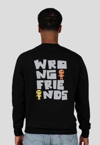 Zwart sweatshirt met de tekst "WRONG FRIENDS" in het grijs en cartoonfiguren in het geel en oranje. Zacht materiaal, ronde hals en geribde manchetten.