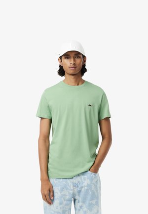 T-shirt en coton vert clair à manches courtes et col rond, arborant un petit logo brodé. Associé à un jean à motifs bleu clair.
