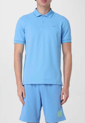 Polo shirt azzurro chiaro con maniche corte, colletto e un piccolo logo; abbinato a pantaloni corti coordinati con un'accento verde con il numero "68".