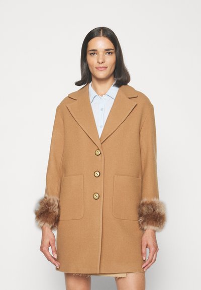 Cappotto in lana cammello con ampi revers, tre bottoni, due tasche frontali e dettagli in pelliccia sui polsini. Texture liscia e vestibilità sartoriale.
