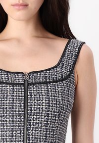 Robe en tweed bleu marine et blanc avec un décolleté carré, une finition noire et un zip à l'avant. Tissu texturé avec un motif tissé.