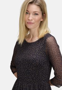 Marineblaues Polka-Dot-Kleid mit transparenten langen Ärmeln, runder Halslinie und gerafftem Bund. Strukturierter Stoff mit einem verspielten Muster.