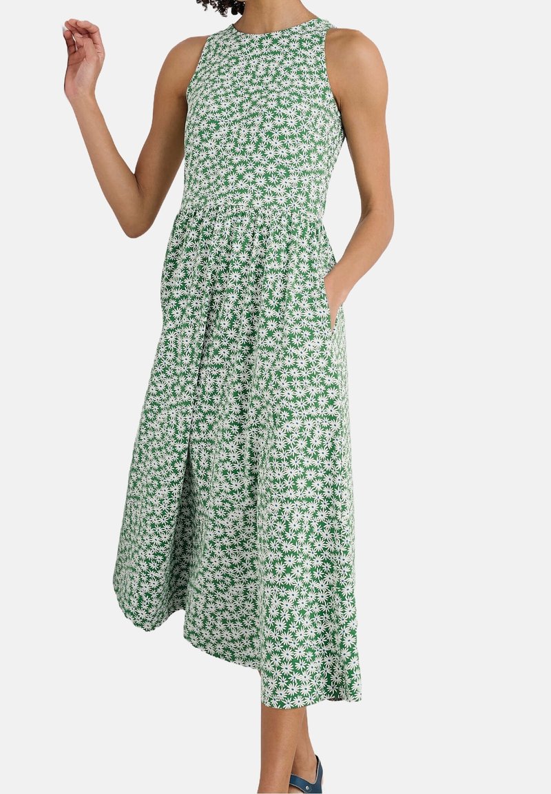Robe midi verte sans manches avec imprimé marguerites blanches, taille cintrée, encolure ronde, poches latérales, portée avec des chaussures plates bleues.