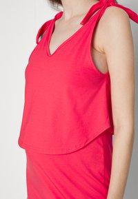 Top sem mangas em fúcsia com decote em V e alças amarradas, feito de um tecido macio. Apresenta um corte descontraído e uma bainha traseira ligeiramente mais longa.