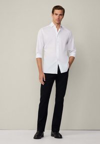 Witte button-up shirt met lange mouwen, zwarte broek en zwarte schoenen. Het shirt heeft een klassieke kraag en een slim fit ontwerp.