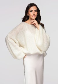 Pull en maille ivoire surdimensionné et doux avec une finition texturée et des manches larges, associé à une jupe en satin lisse de couleur claire.