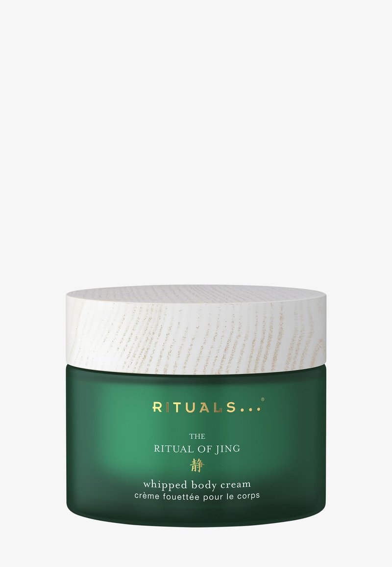 Bocal en verre vert avec un couvercle en bois blanc texturé, portant le texte doré "RITUELS... LE RITUEL DE JING crème corporelle fouettée" en plusieurs langues.