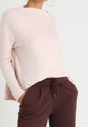 Ljusrosa, långärmad topp med avslappnad passform, mjuk textur och hög krage. Matcher med mörkbruna byxor med snörning och veck.