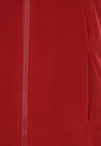 Röd fleecejacka med centralsdragkedja, slät textur och figursydd design. Tyget verkar varmt och mjukt.