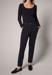 Pantalon bleu marine ajusté avec une coupe slim, fermeture à boutons sur le devant, poches latérales, associé à un haut à manches longues foncé et des chaussures tissées noires sans lacets.