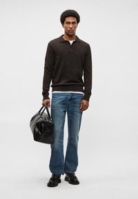 Σκούρος καφέ πλεκτός πουλόβερ, ανοιχτό γαλάζιο τζιν, μαύρα παπούτσια, κρατώντας μια υφασμάτινη μαύρη τσάντα με χερούλια. Άσπρο μπλουζάκι ορατό στη μέση.